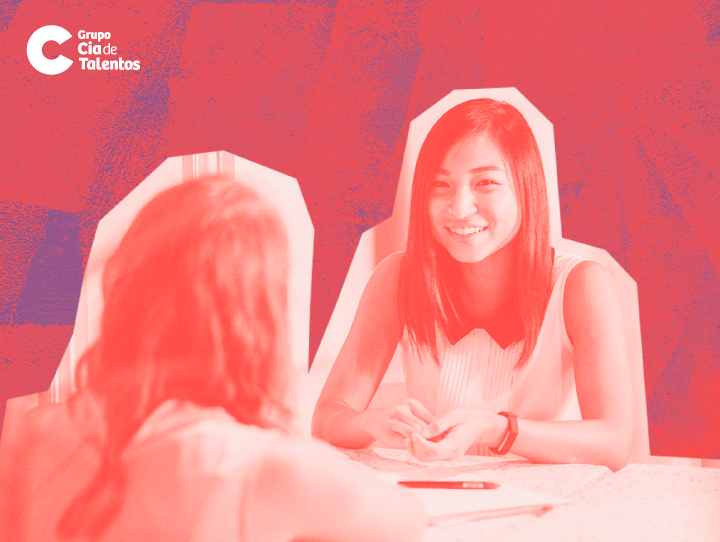 A imagem do artigo: Como se dar bem na fase de entrevista apresenta duas pessoas, sentadas à mesa, conversando. Uma delas, de cabelo liso e comprido e está de costas, enquanto a outra, é uma jovem oriental. Ela sorri e possui cabelos escuros, lisos e médios e veste uma blusa branca. A imagem toda possui um filtro avermelhado e a logomarca Grupo Cia de Talentos está no canto superior esquerdo.