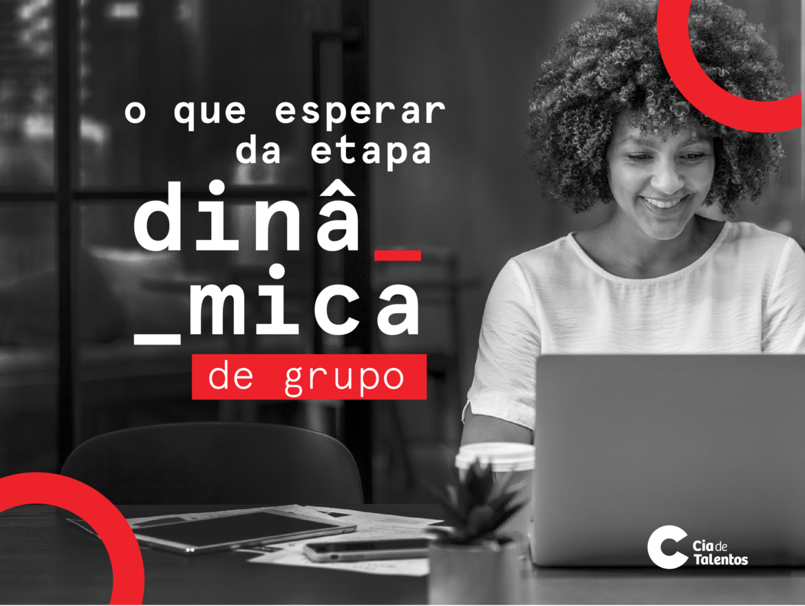 a imagem que ilustra o artigo O que esperar da etapa dinâmica de grupo traz uma foto em preto e branco de uma mulher negra de cabelos cacheados. Ela sorri enquanto olha para a tela de um laptop. Ela está sentada em uma mesa que também contém um caderno, uma caneta e uma planta pequena.